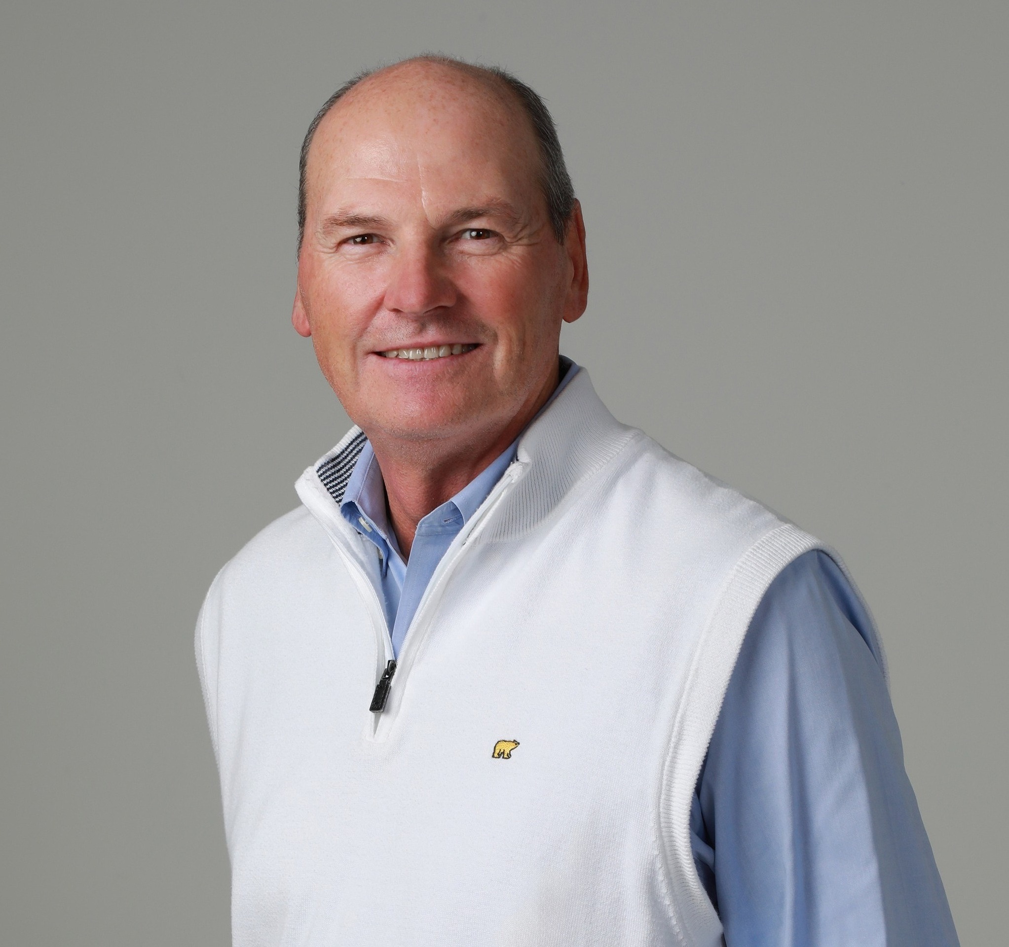 Larry Grill standing with hands in pockets and smiling against gray background.